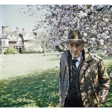 Photograph of Collingwood Ingram in hat stood under a blossom tree